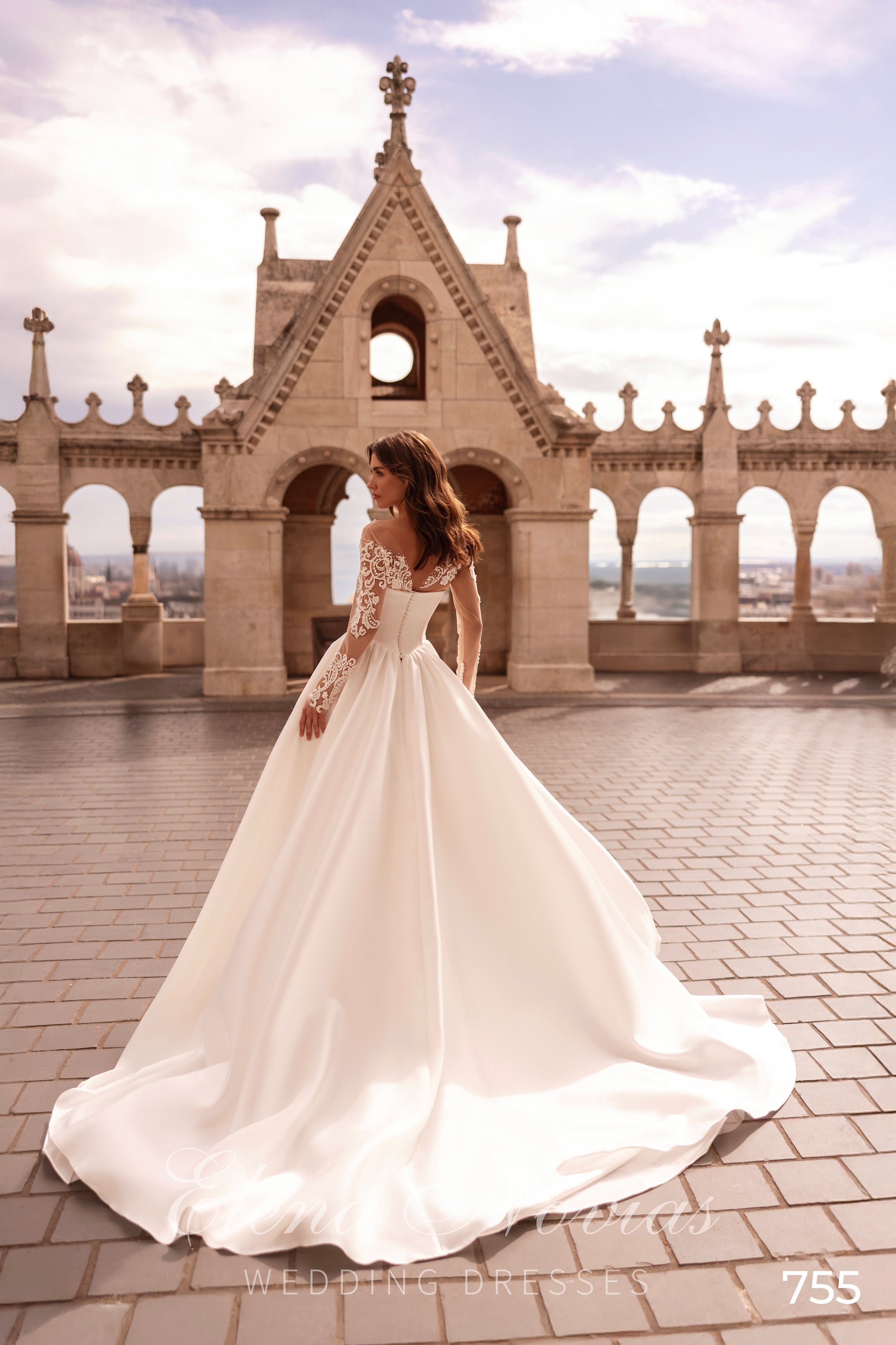 Flowing ivory wedding dress with sheer lace sleeves and a long, wide train seen from the back