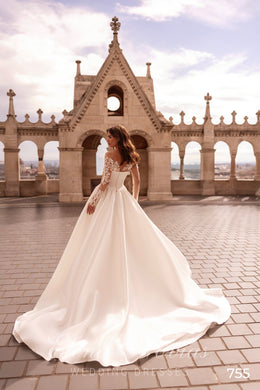 Flowing ivory wedding dress with sheer lace sleeves and a long, wide train seen from the back
