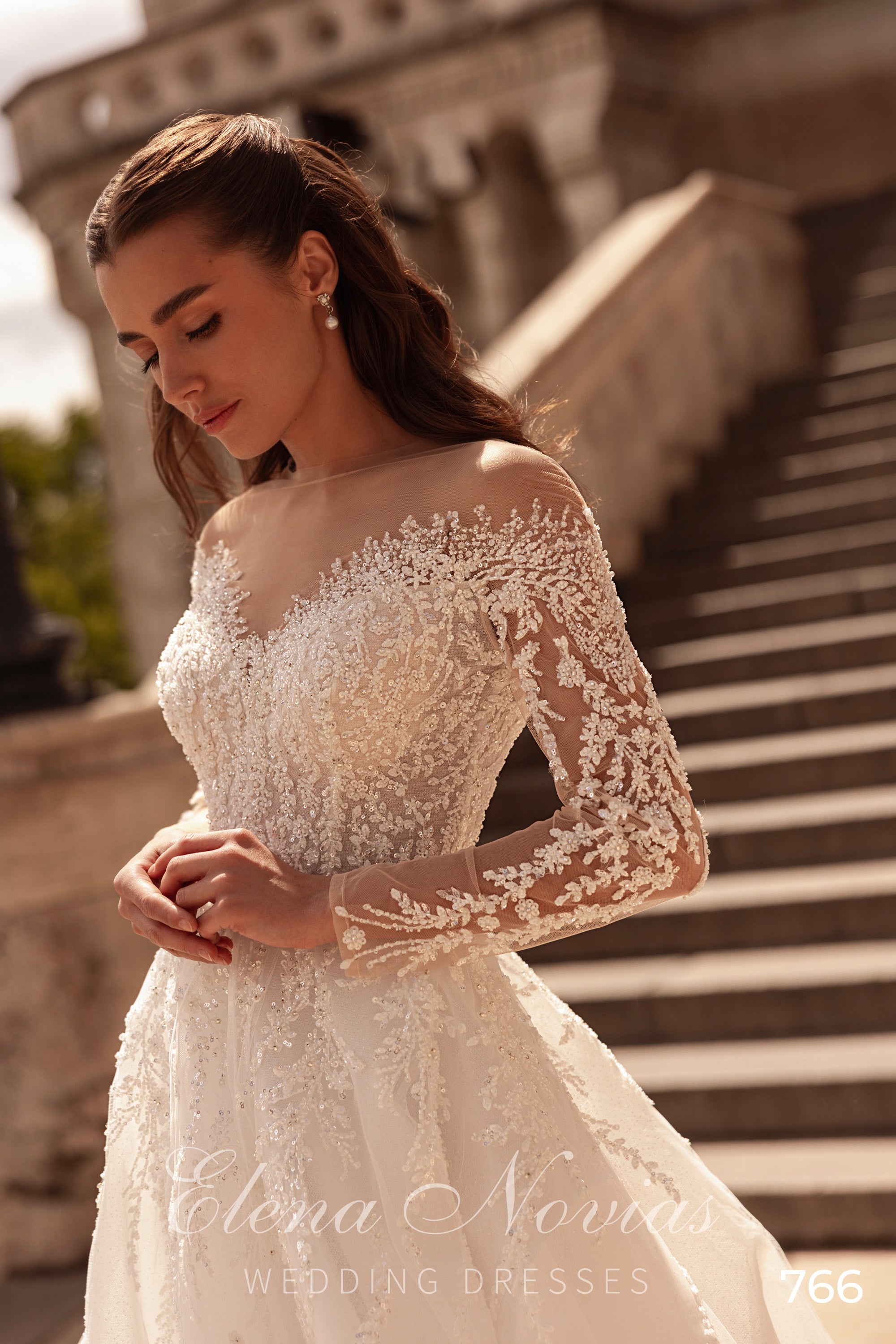 Ivory wedding dress with a sheer bateau neckline, long floral lace sleeves, and beaded lace bodice
