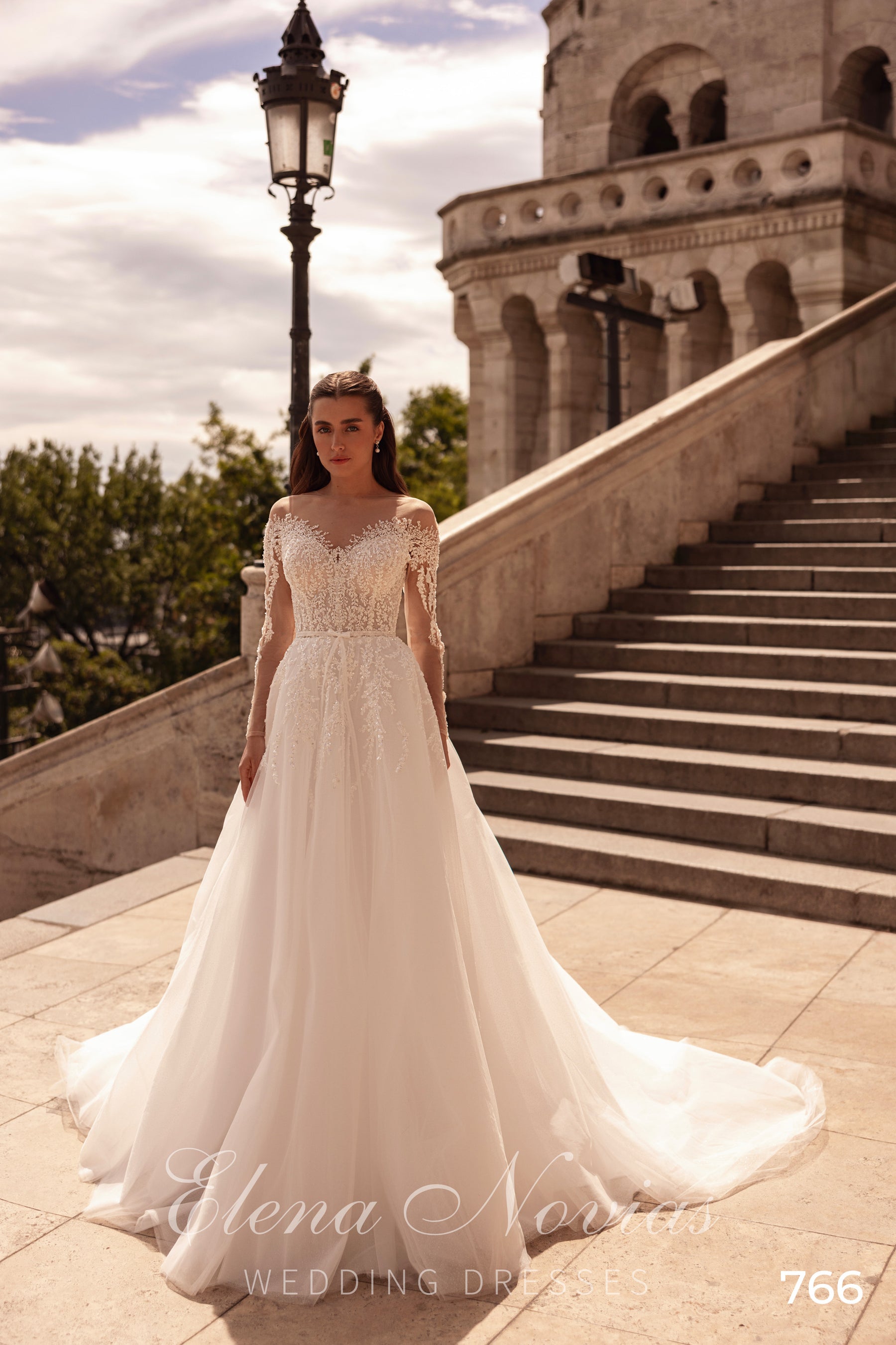 Full-length ivory A-line wedding dress with a sheer lace bodice, long sleeves, and a flowing train