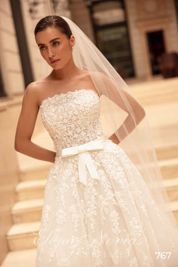 Close-up of an ivory strapless wedding dress with dense pearl beadwork, waist bow, and patterned A-line skirt