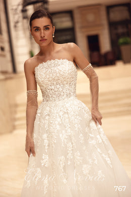 Strapless ivory wedding dress featuring a heavily beaded bodice, bow belt, and floral-patterned A-line skirt