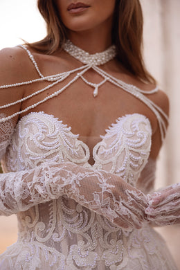 Close-up of floral beadwork, lace sleeves, and pearl straps on an ivory wedding dress bodice