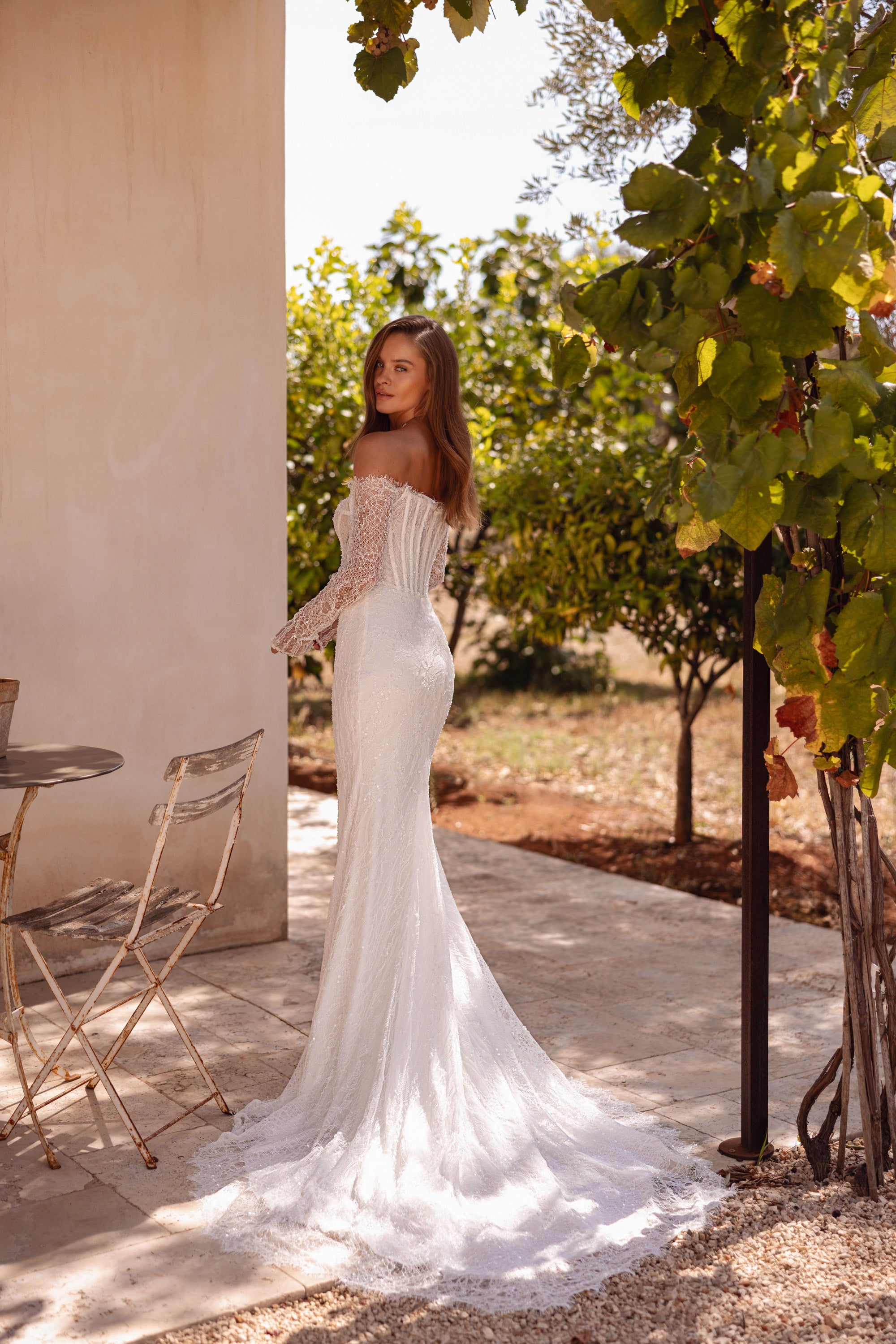 Side view of an ivory mermaid wedding dress with lace sleeves and a long, spread-out train