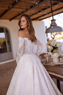 Three-quarter back view of an ivory lace wedding dress with long sleeves, a fitted waist, and flowing train
