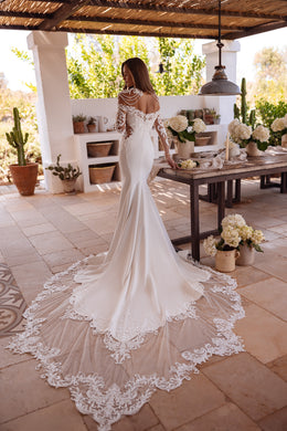 Rear view of an ivory mermaid wedding dress with an open back, lace sleeves, and an ornate floor-length train