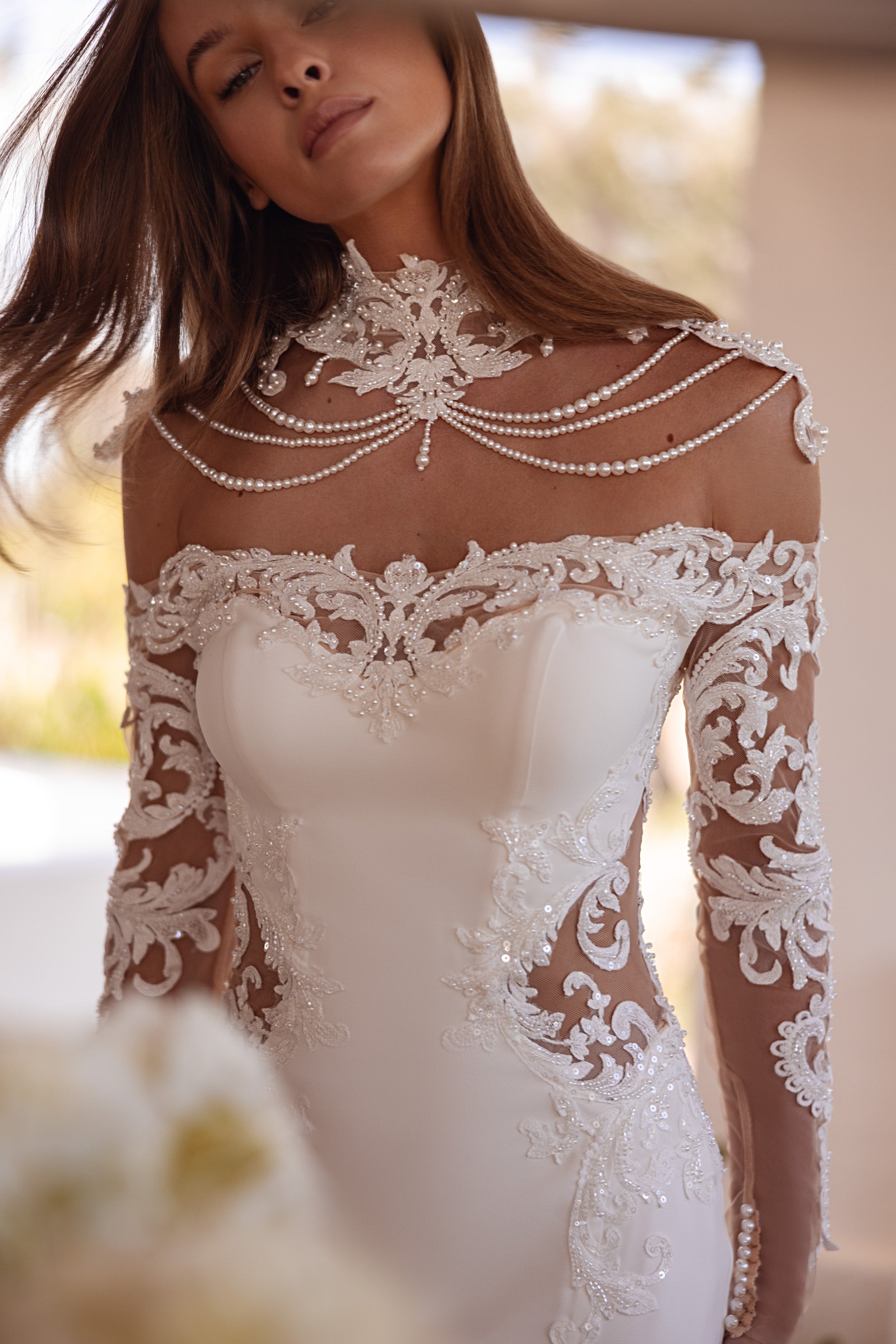 Close-up of an ivory wedding dress neckline with floral lace appliqué, sheer sleeves, and draped beadwork