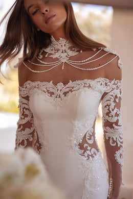 Close-up of an ivory wedding dress neckline with floral lace appliqué, sheer sleeves, and draped beadwork