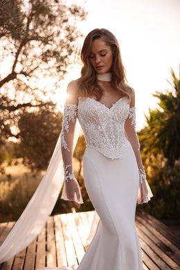 Ivory sheath wedding dress with a beaded lace sweetheart bodice, sheer long sleeves, and a trailing cape