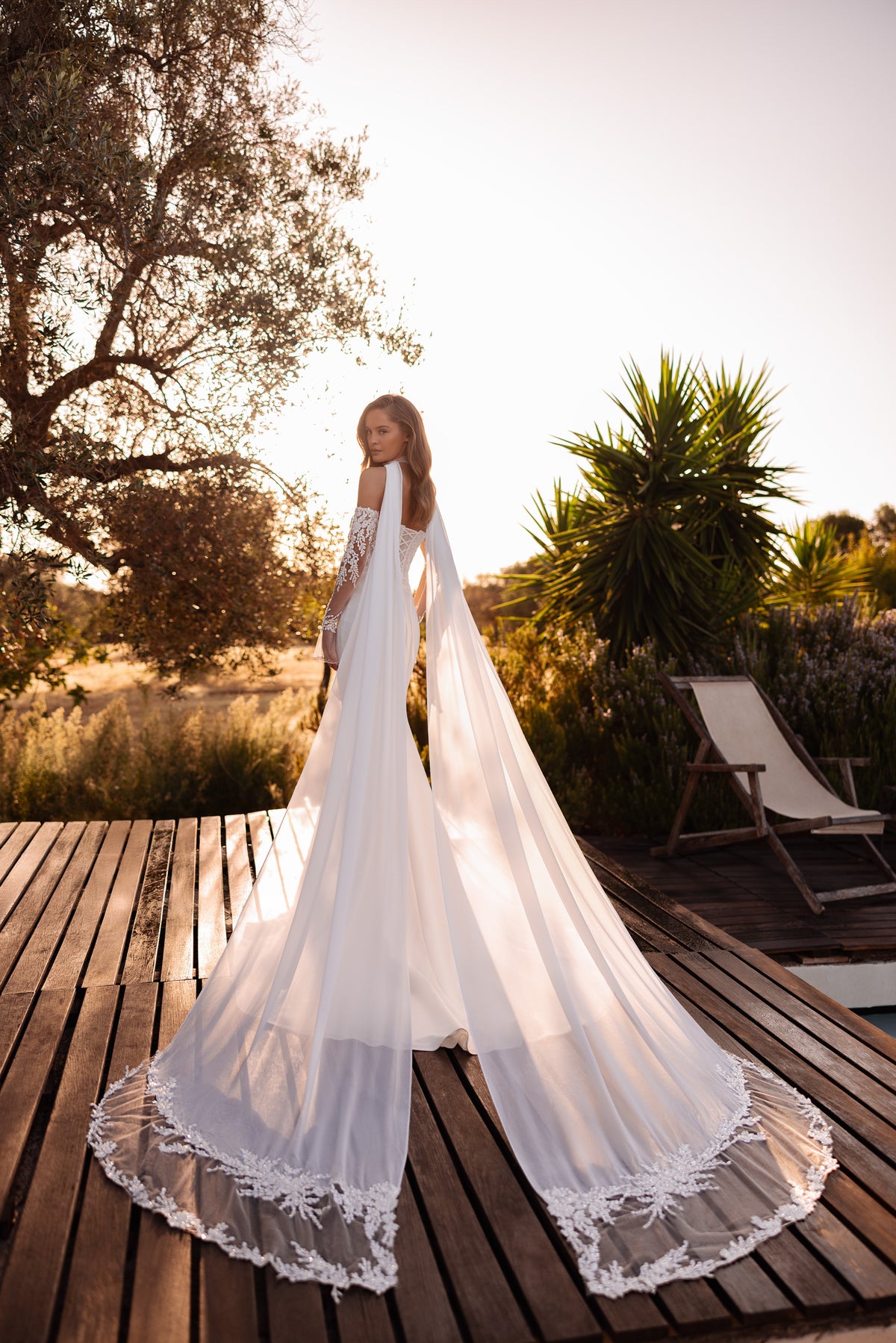 Rear view of an ivory wedding dress with a long sheer cape edged in floral lace and a flowing train