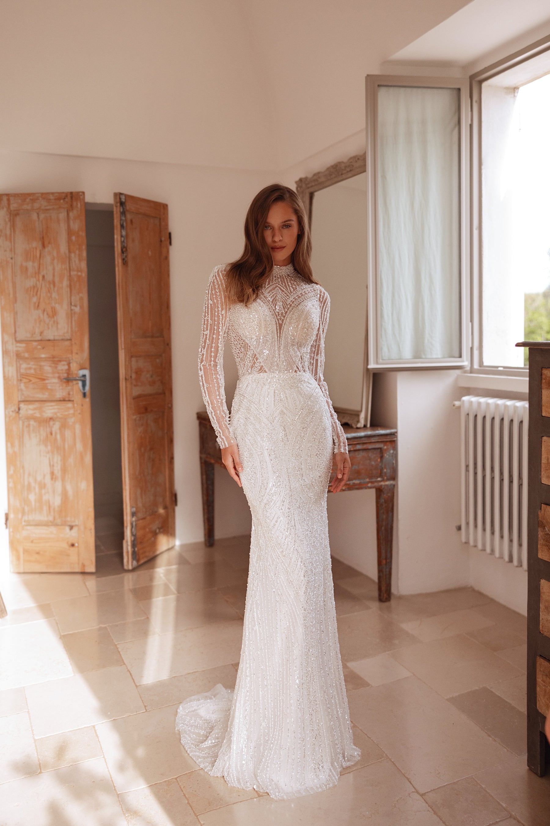 Full-length ivory wedding dress with a fitted sheath silhouette, long sleeves, and sweeping train