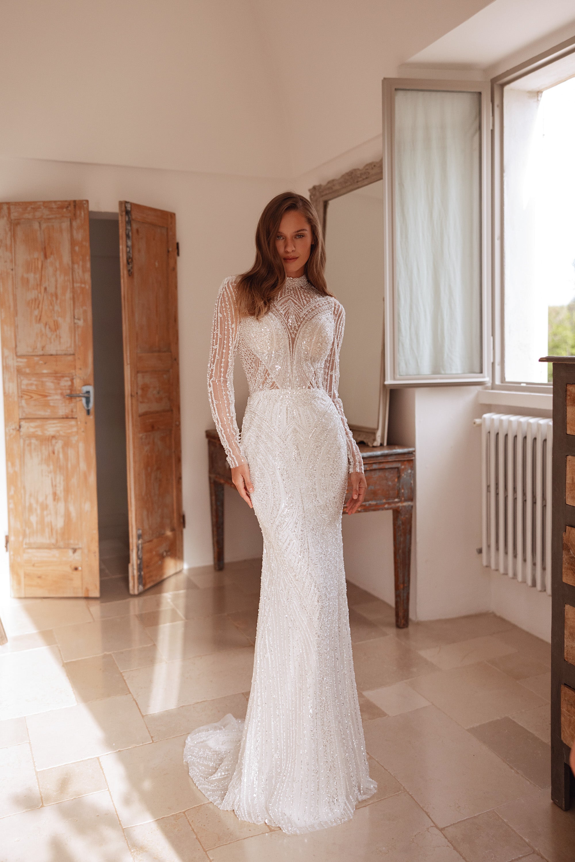 Full-length ivory wedding dress with a fitted sheath silhouette, long sleeves, and sweeping train
