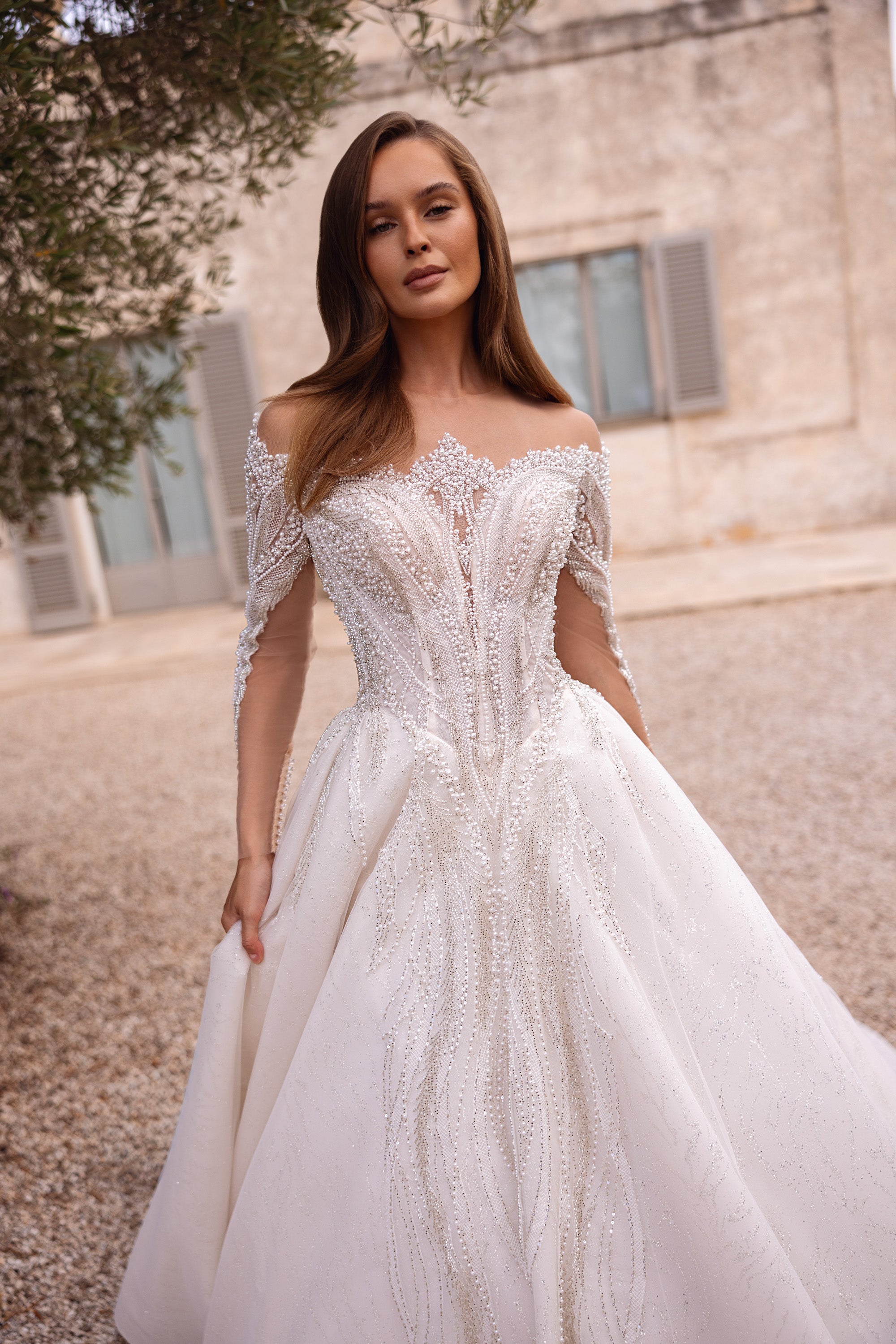 Ivory ball gown wedding dress with an off-shoulder neckline, long sheer sleeves, and sparkling beadwork
