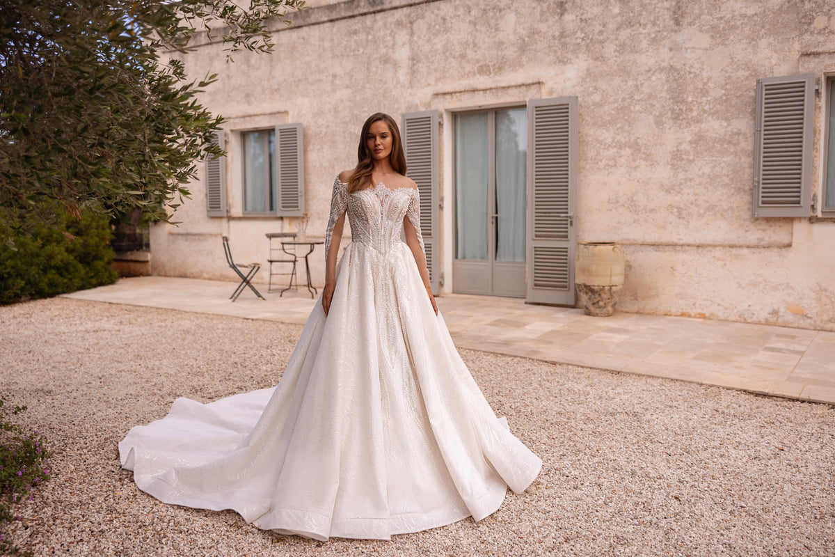 Full ivory wedding dress with a beaded off-shoulder bodice, long sleeves, and a sweeping train
