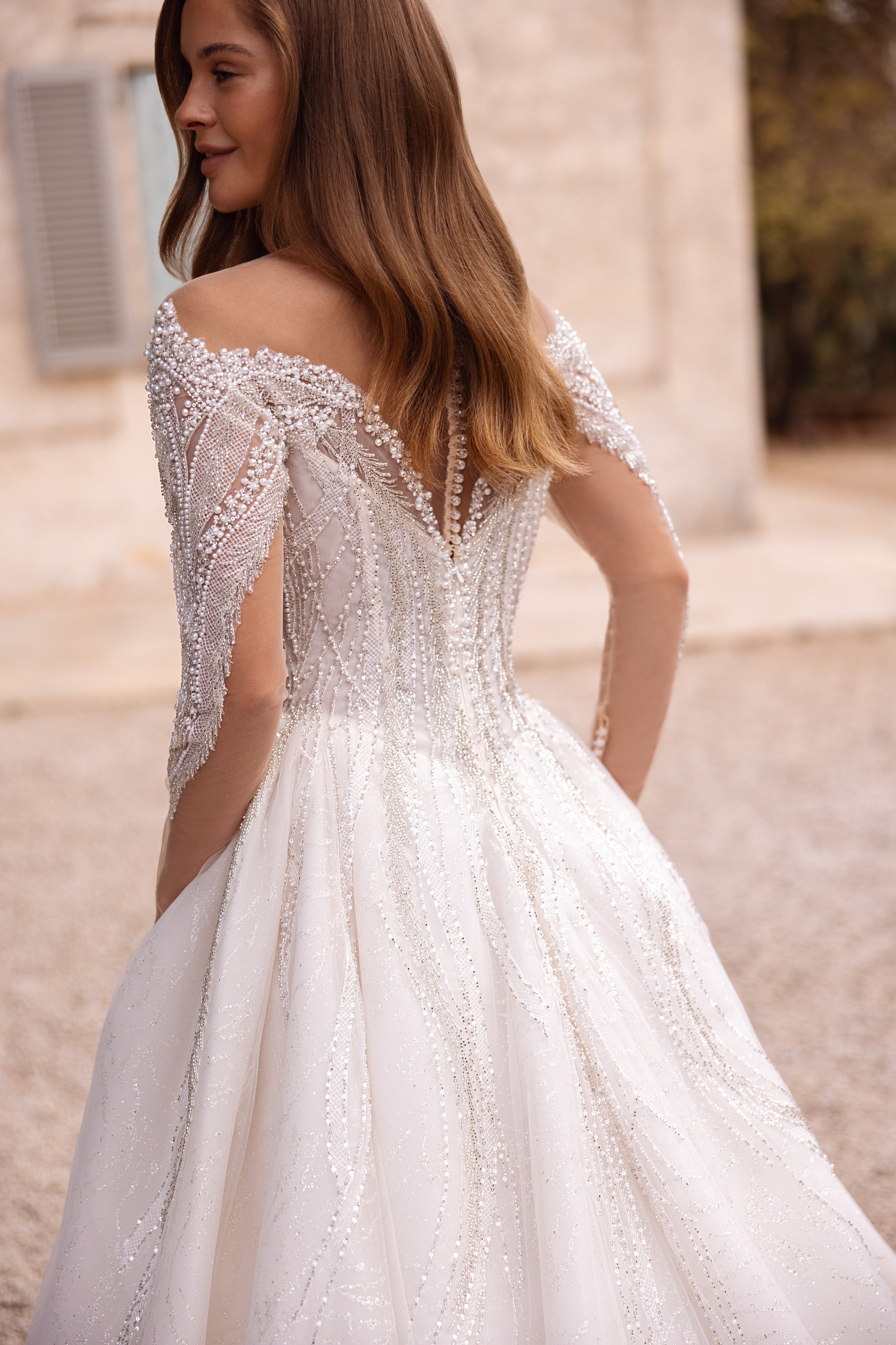 Back view of an ivory wedding dress with beaded long sleeves, a decorated back, and a full flowing skirt