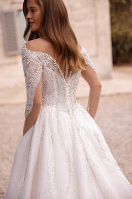 Back view of an ivory wedding dress with beaded long sleeves, a decorated back, and a full flowing skirt