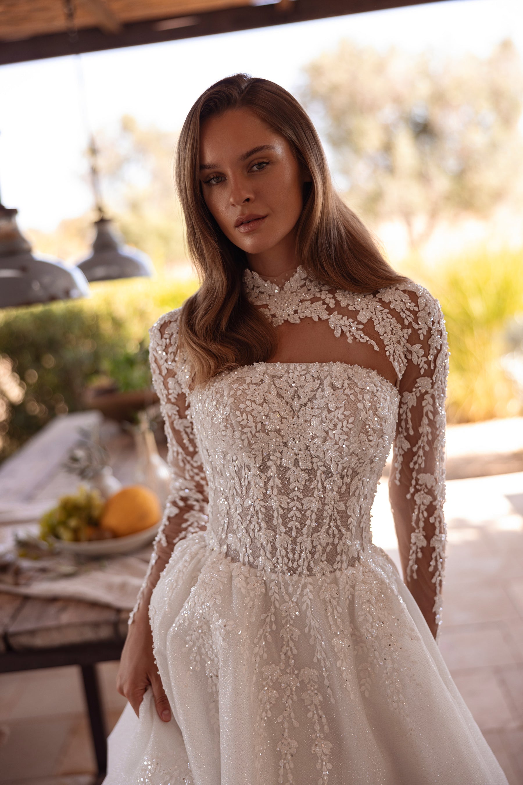 Close-up of an ivory wedding dress bodice with floral lace, beadwork, sheer long sleeves, and a high neckline