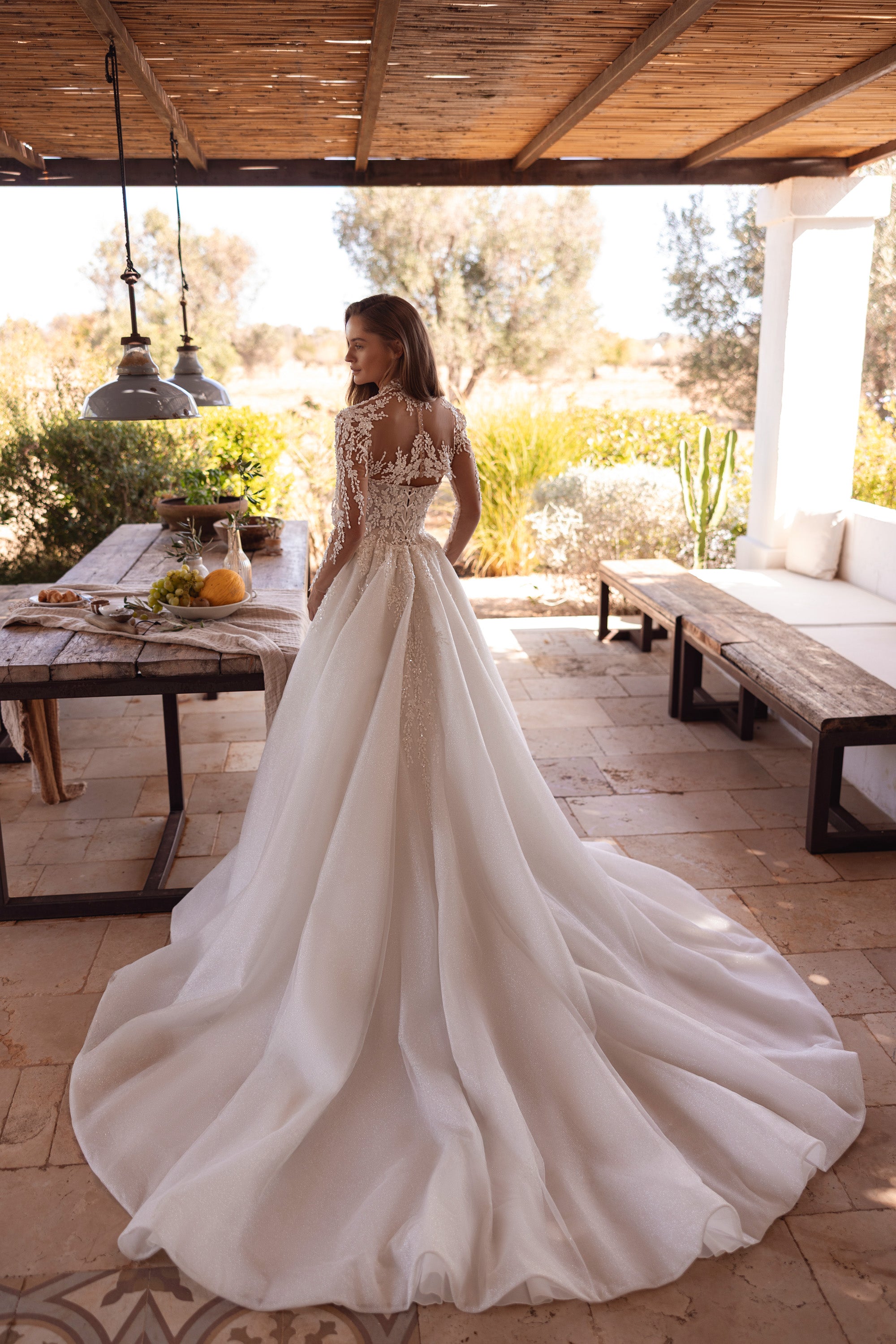 Ivory A-line wedding dress showing a sheer lace back, long sleeves, defined waist, and an extended train