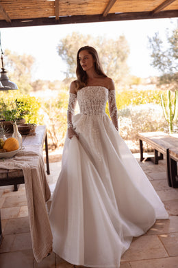 Ivory A-line wedding dress with an off-the-shoulder neckline, lace sleeves, and a glittering fitted bodice