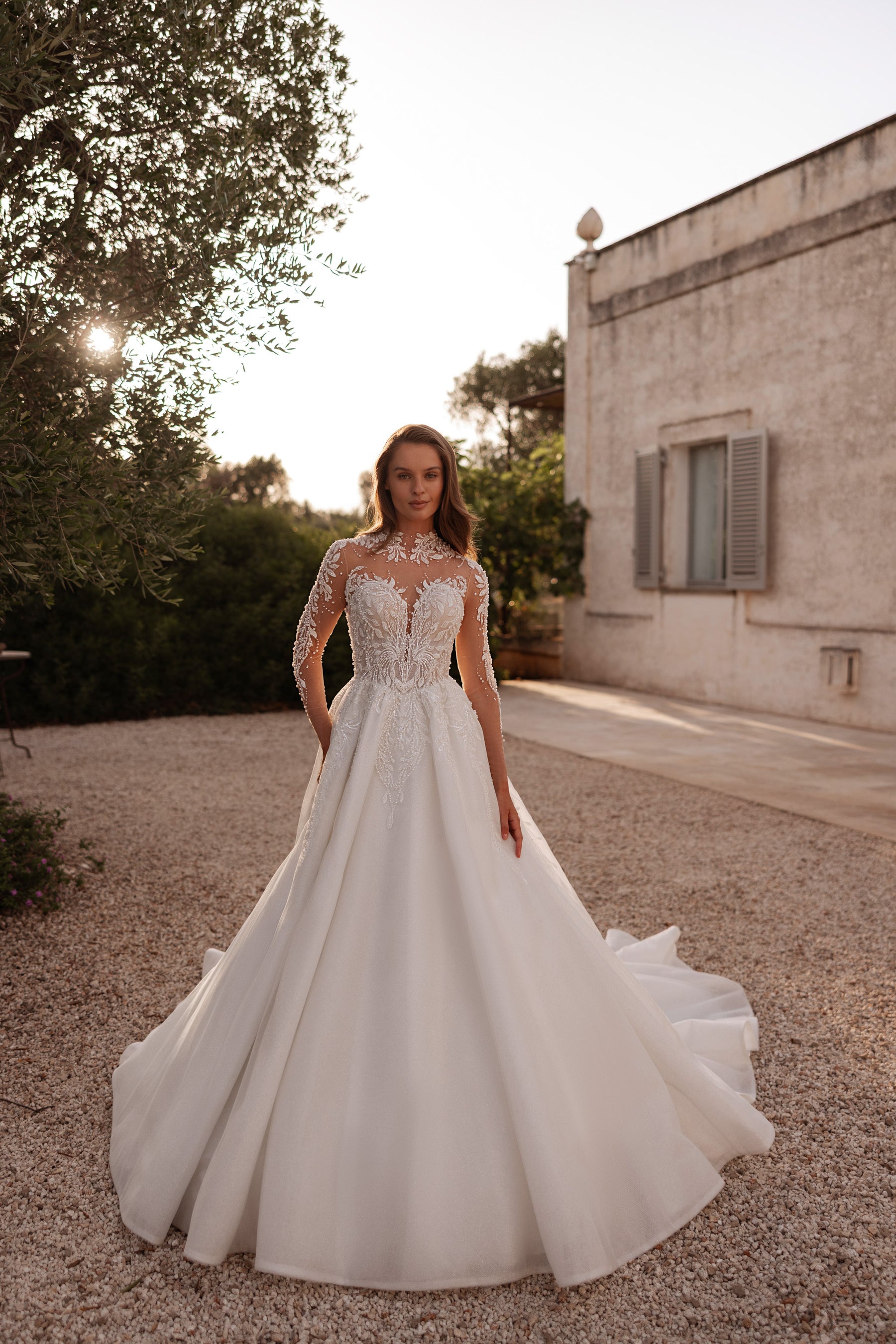 Ivory A-line wedding dress with an illusion high neckline, long sleeves, beaded lace bodice, and flowing train