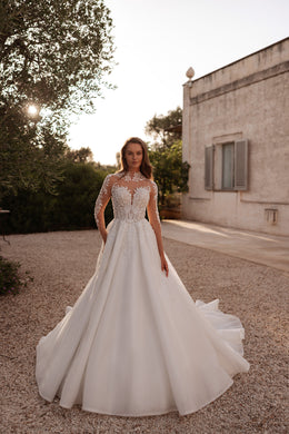 Ivory A-line wedding dress with an illusion high neckline, long sleeves, beaded lace bodice, and flowing train