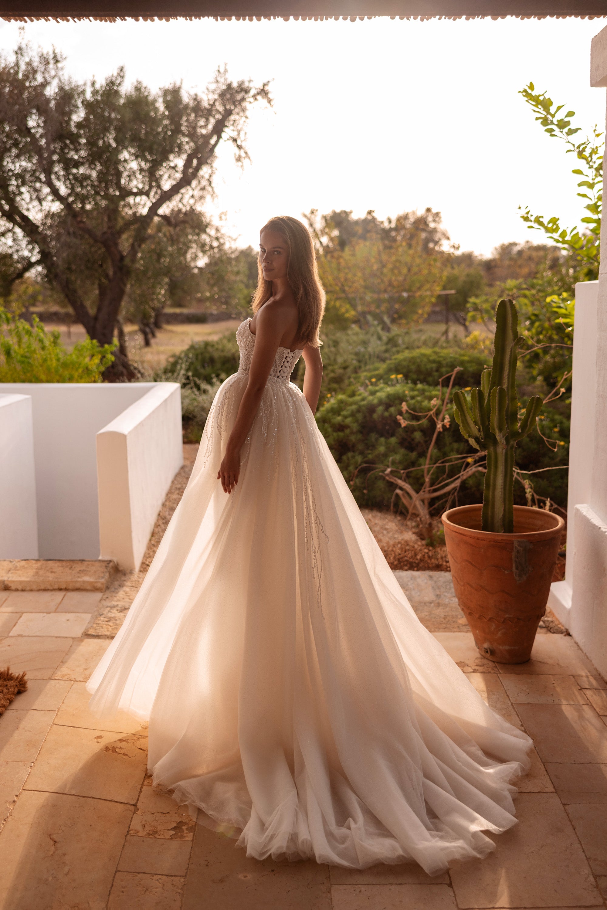 Side view of an ivory wedding dress with a fitted beaded gown beneath a sheer tulle overskirt and train