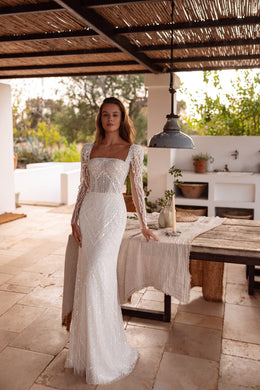 Square-neck beaded wedding dress with sheer long sleeves and a slim silhouette ending in a short train