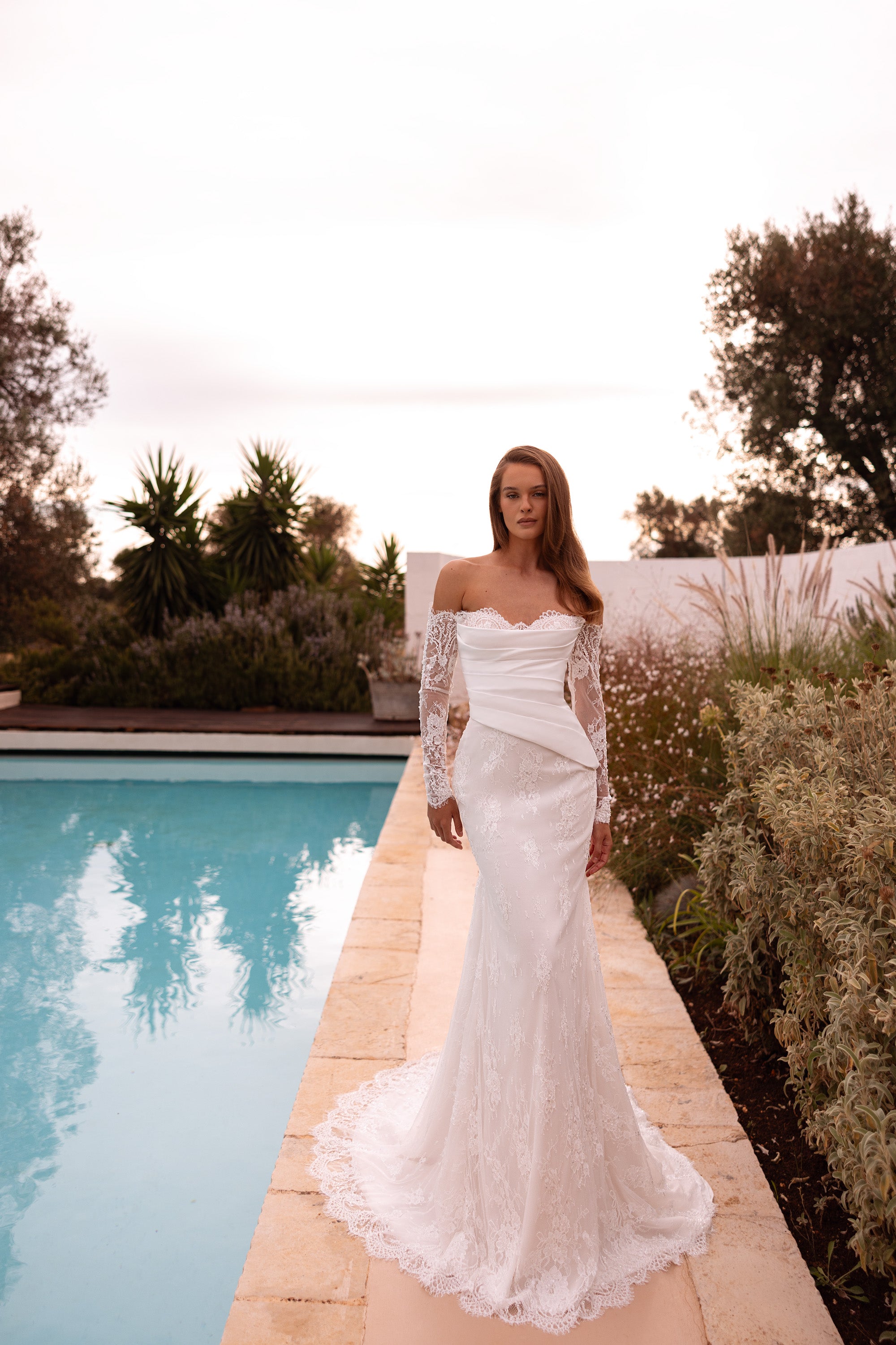 Ivory mermaid wedding dress with an off-shoulder neckline, lace sleeves, floral lace skirt, and scalloped hem