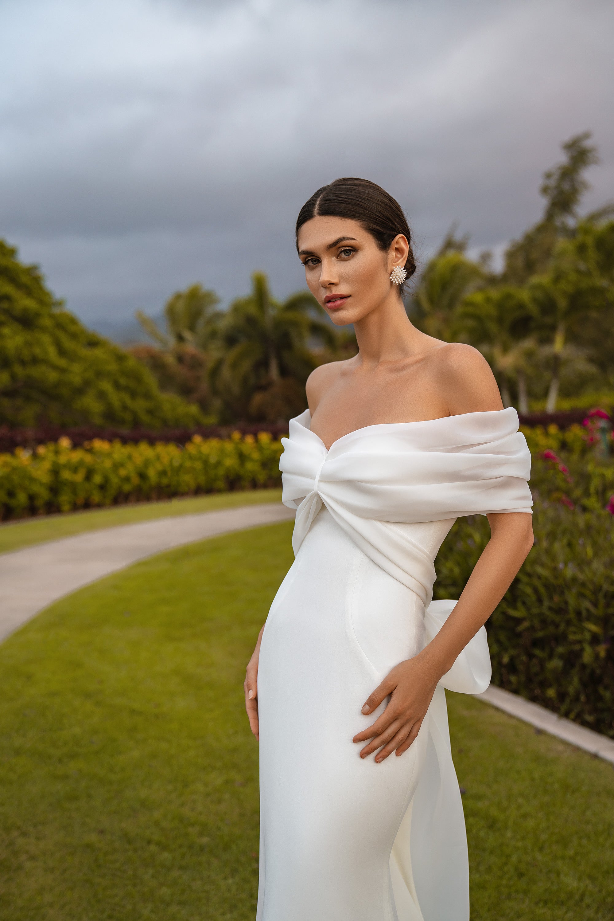 Close-up of an ivory wedding dress with a twisted off-the-shoulder neckline, draped sleeves, and fitted bodice