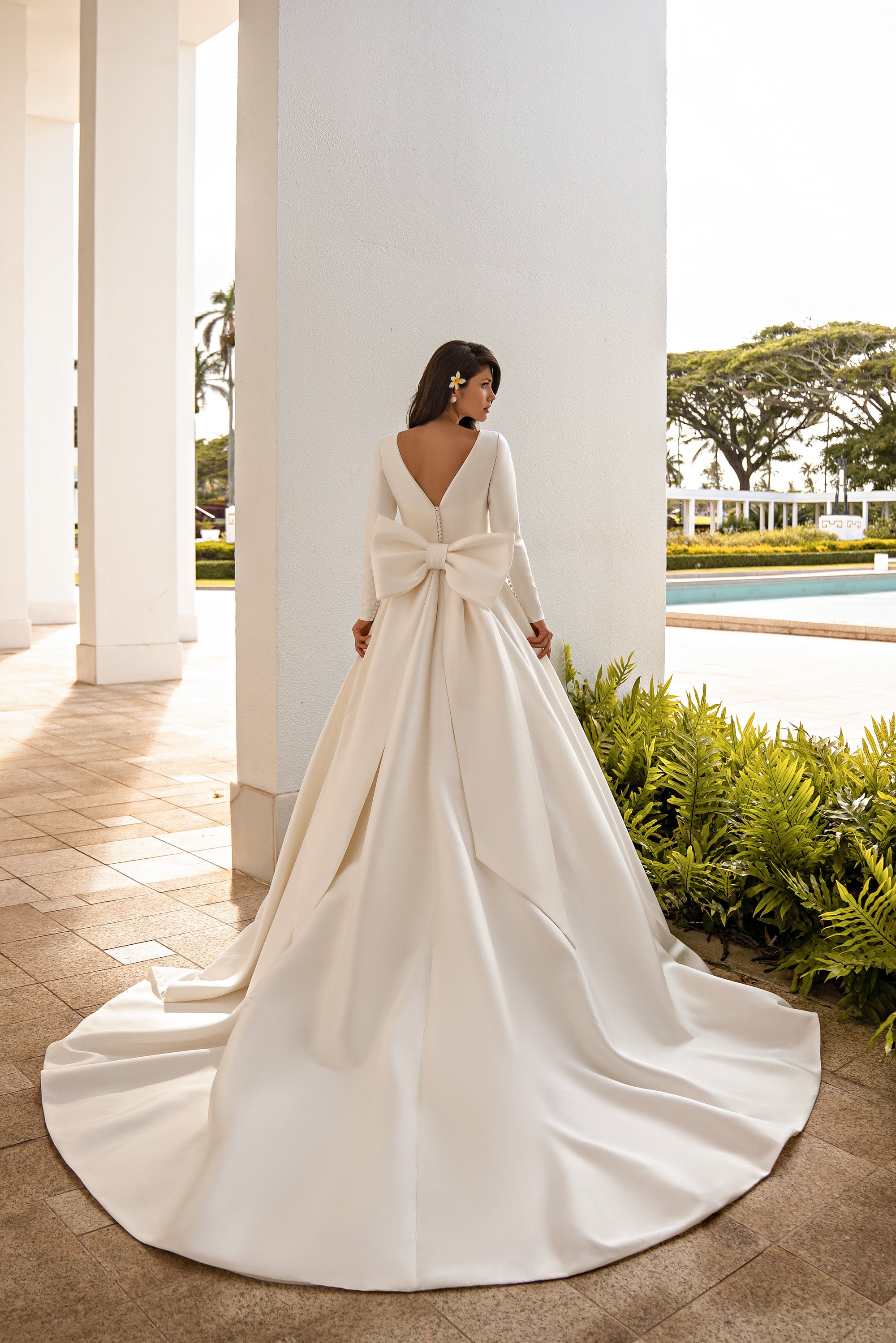 Ivory wedding dress with long sleeves, a large back bow, and a wide sweeping train