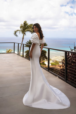 White satin wedding dress showing a fitted mermaid silhouette, draped back neckline, and long flowing train