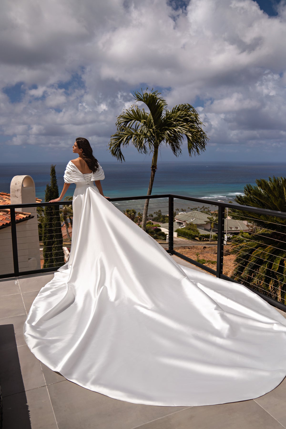 Back view of a white satin wedding dress with a tied waist bow and dramatic floor-spreading overskirt