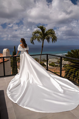 Back view of a white satin wedding dress with a tied waist bow and dramatic floor-spreading overskirt