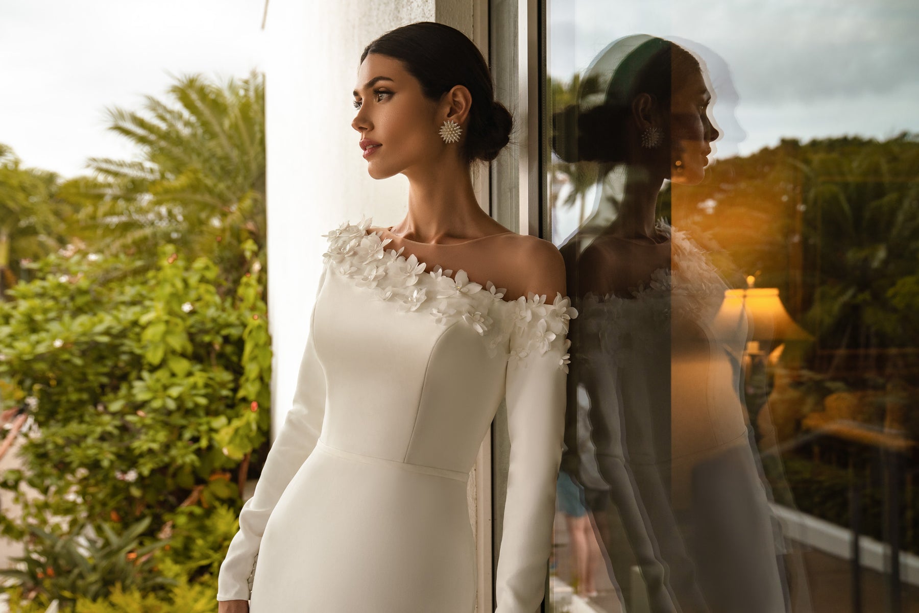 Close-up of an ivory wedding dress with long sleeves and three-dimensional floral appliqués at the neckline