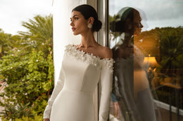 Close-up of an ivory wedding dress with long sleeves and three-dimensional floral appliqués at the neckline