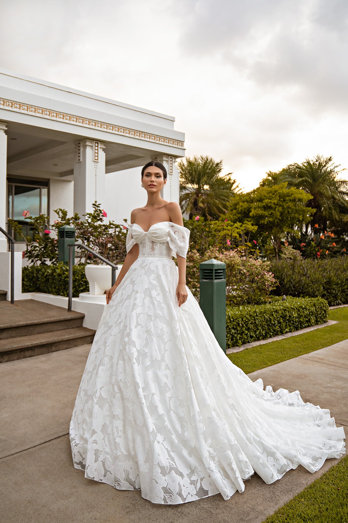 White floral lace ball gown wedding dress with an off-the-shoulder bow and sweeping train