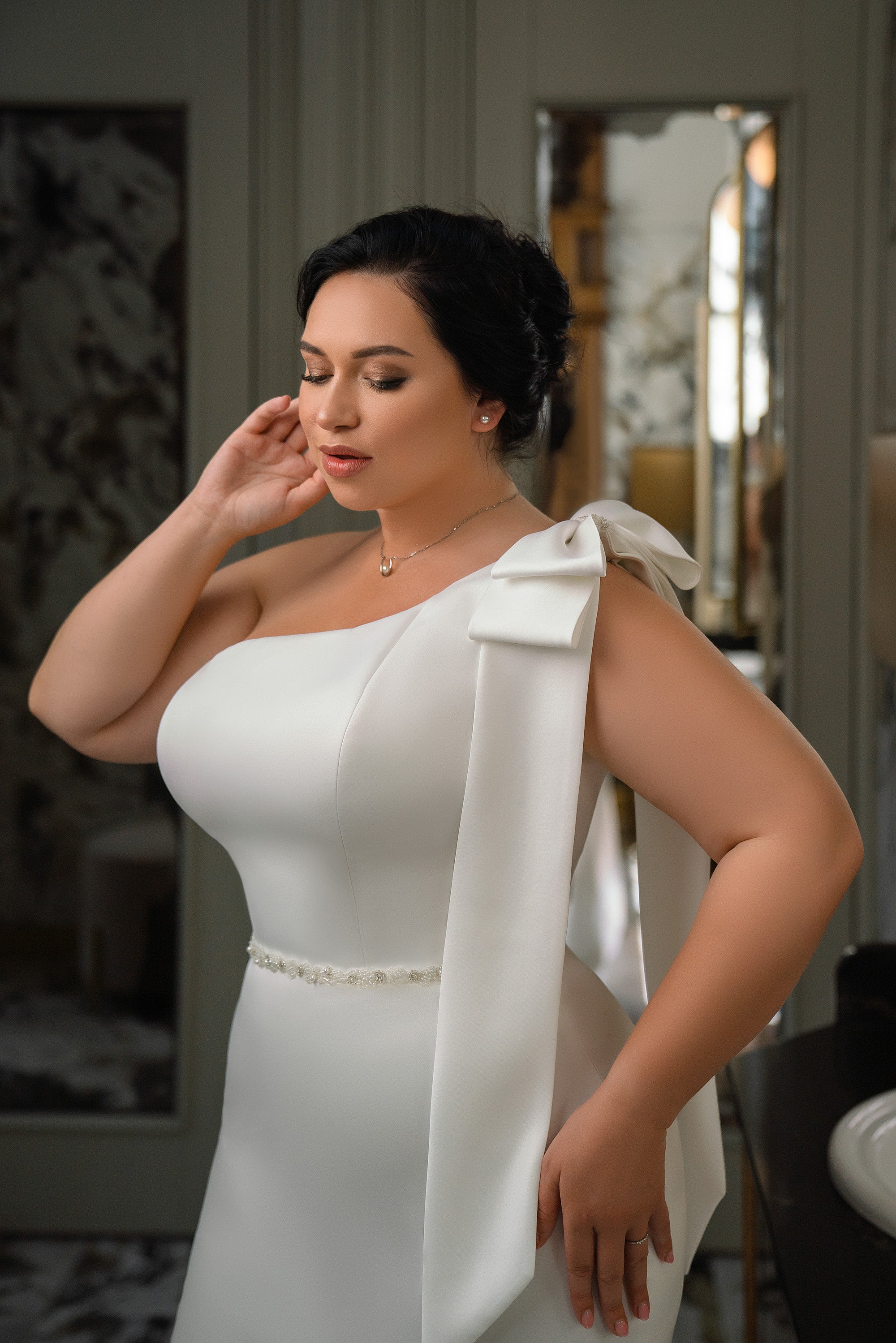 Close-up of an ivory wedding dress with a one-shoulder bow neckline and beaded waist