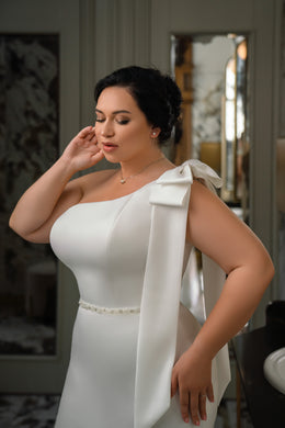Close-up of an ivory wedding dress with a one-shoulder bow neckline and beaded waist
