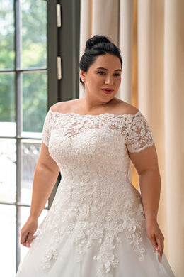 Close-up of an off-the-shoulder ivory wedding dress with short lace sleeves and floral appliqué on the fitted bodice