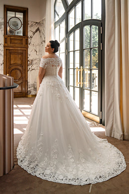 Lace-back ivory wedding dress with floral appliqués, a full ball-gown skirt, and a scalloped sweeping train
