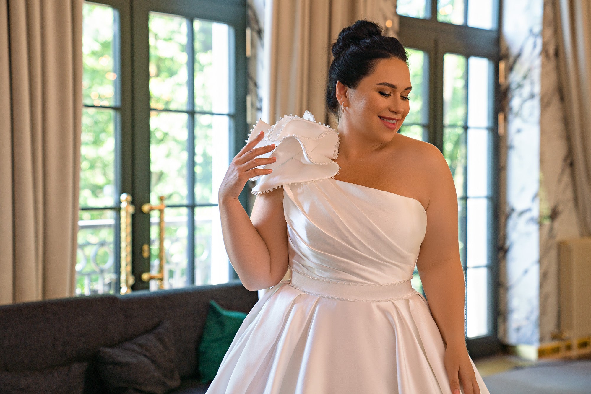Close-up of an ivory one-shoulder wedding dress with a draped bodice, ruffled shoulder, and beaded waist