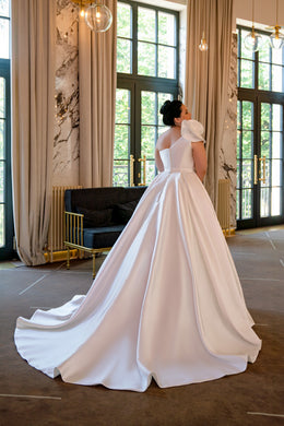 Ivory wedding dress with a fitted bodice, open back, ruffled shoulder detail, and sweeping satin ball-gown train