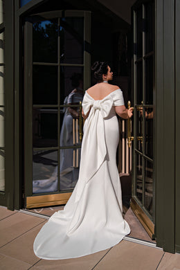 Ivory mermaid wedding dress showing a large back bow, short sleeves, and a sweeping train