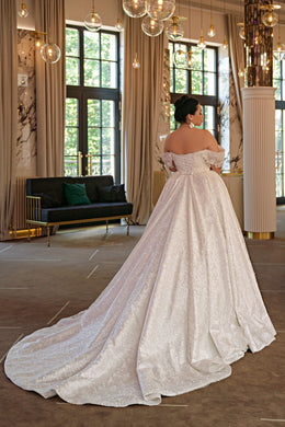 Back view of an ivory wedding dress with an off-shoulder neckline, full ball gown skirt, and long train