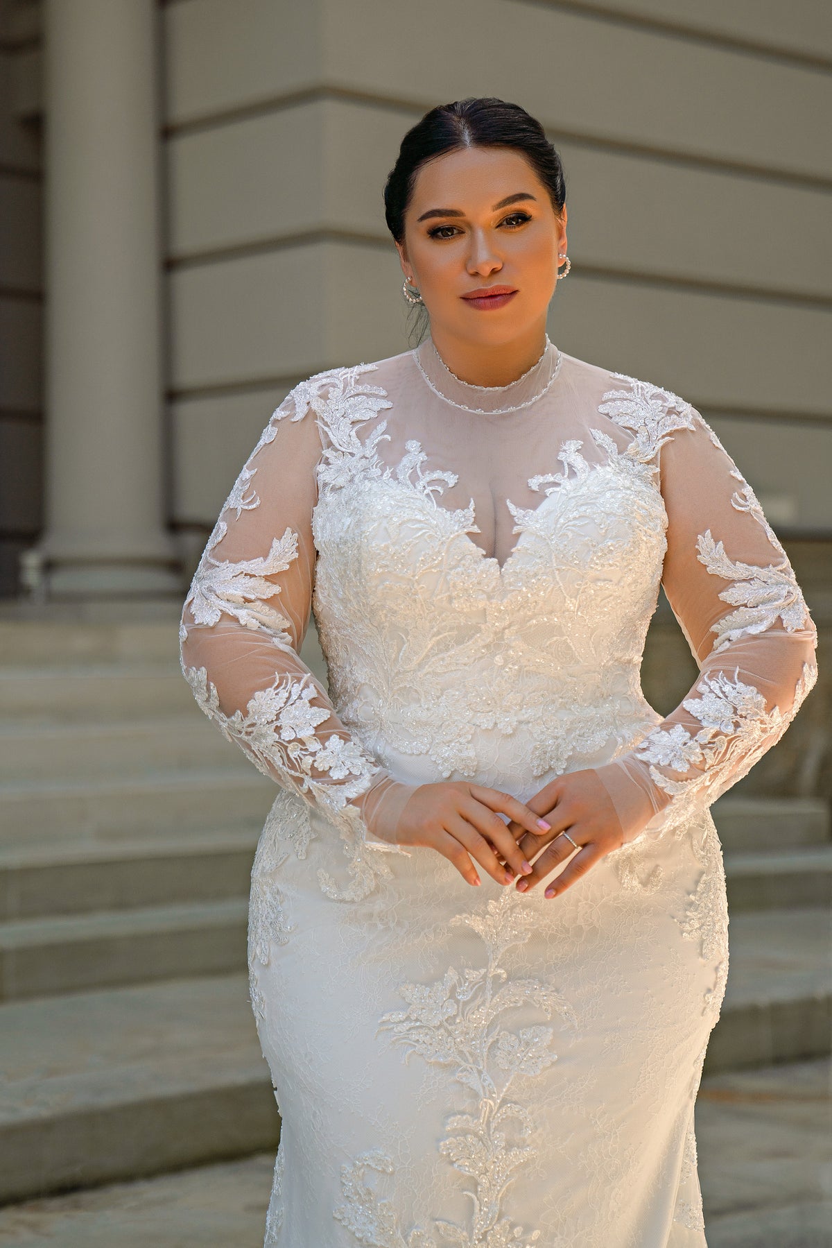 Close-up of an ivory wedding dress with a high illusion neckline, sheer lace sleeves, and floral appliqués