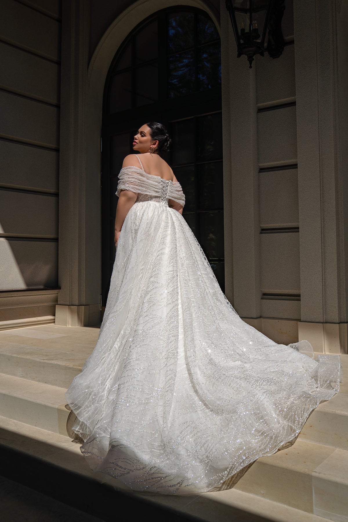 Bare upper back and draped off-shoulder sleeves highlight the glittering train of this ivory wedding dress