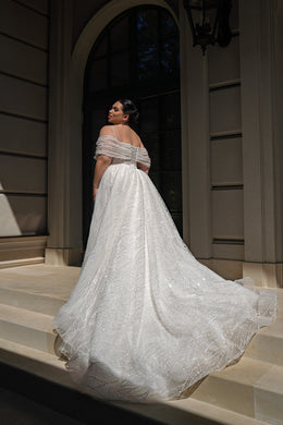 Bare upper back and draped off-shoulder sleeves highlight the glittering train of this ivory wedding dress