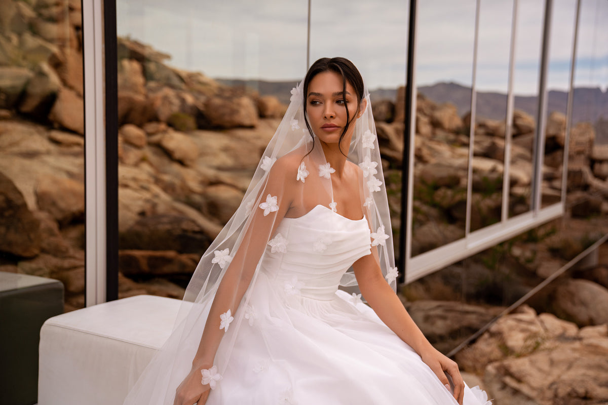 Close-up of an ivory wedding dress with a ruched bodice and sheer floral tulle overlay