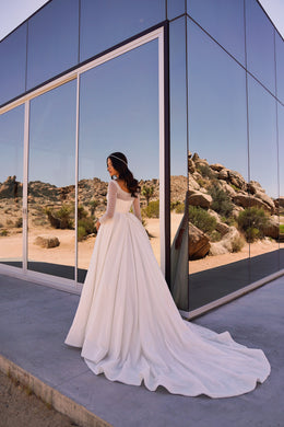 Back view of an ivory wedding dress with long sleeves, a full glittering skirt, and a scalloped train