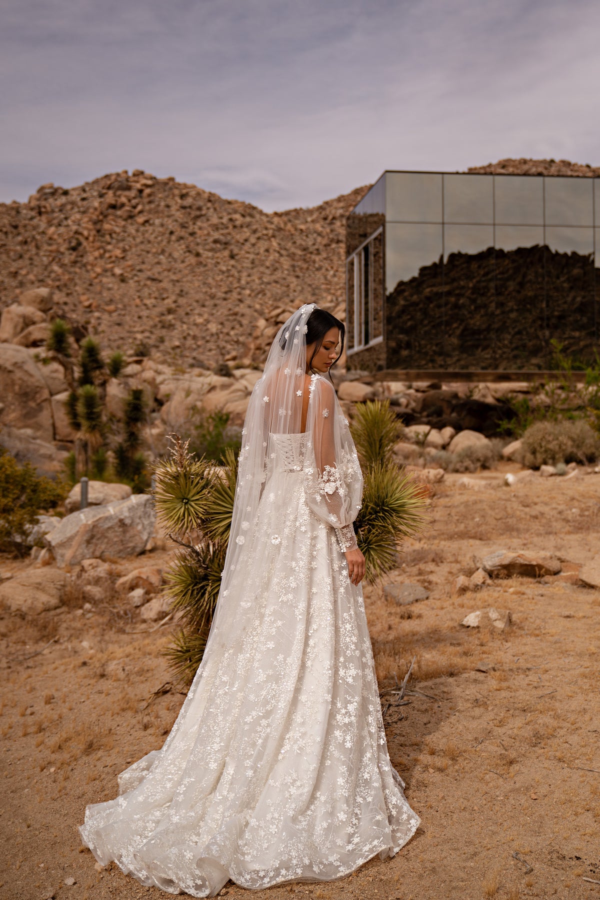 Rear three-quarter view of an ivory wedding dress with a sheer floral-lace back and long lace train